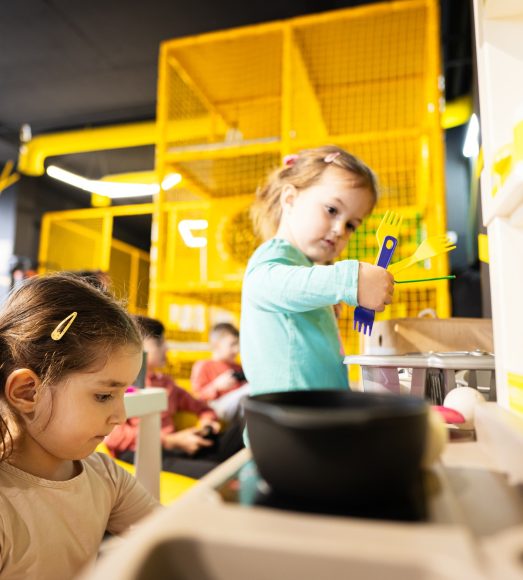 Two sisrers playing in kids kitchen at children play center.